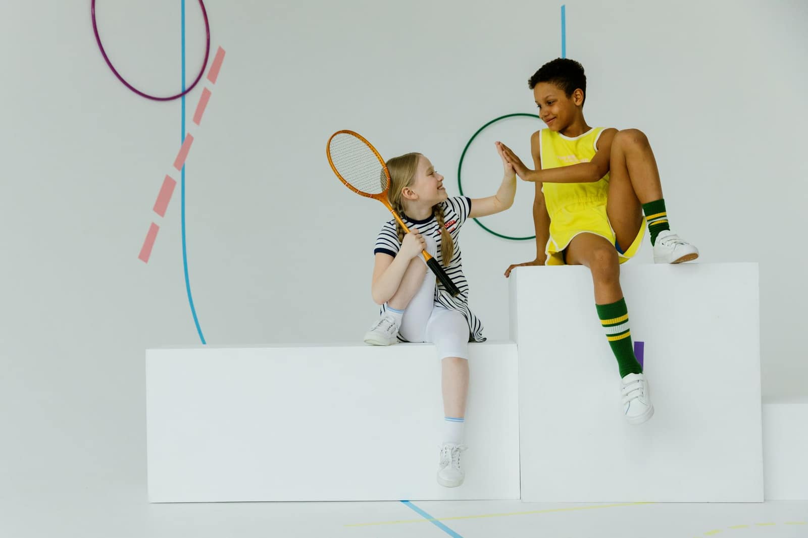 Two children having fun indoors with tennis gear. High-five moment.