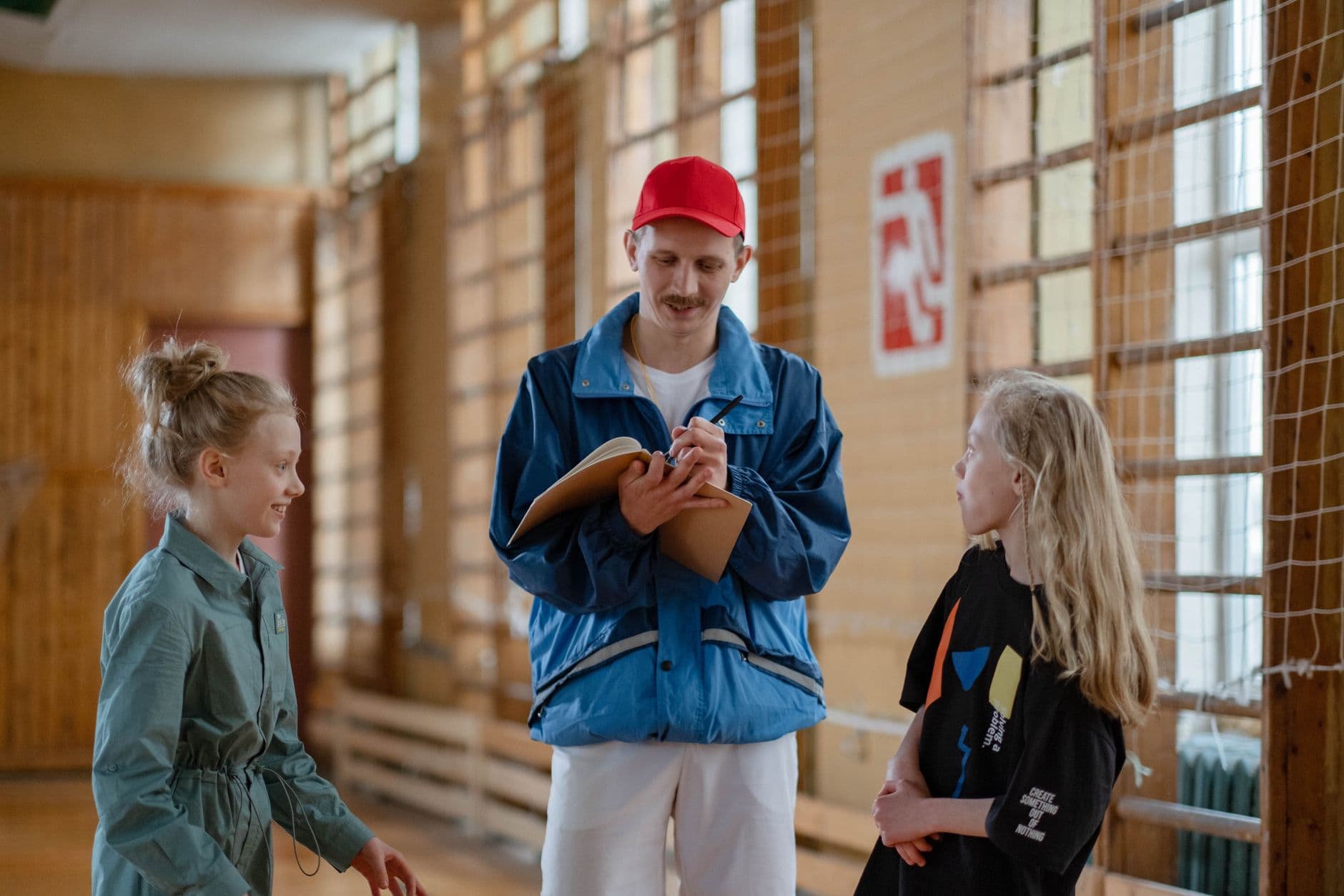 A male coach interacts with two girls during a sports activity in an indoor gym.