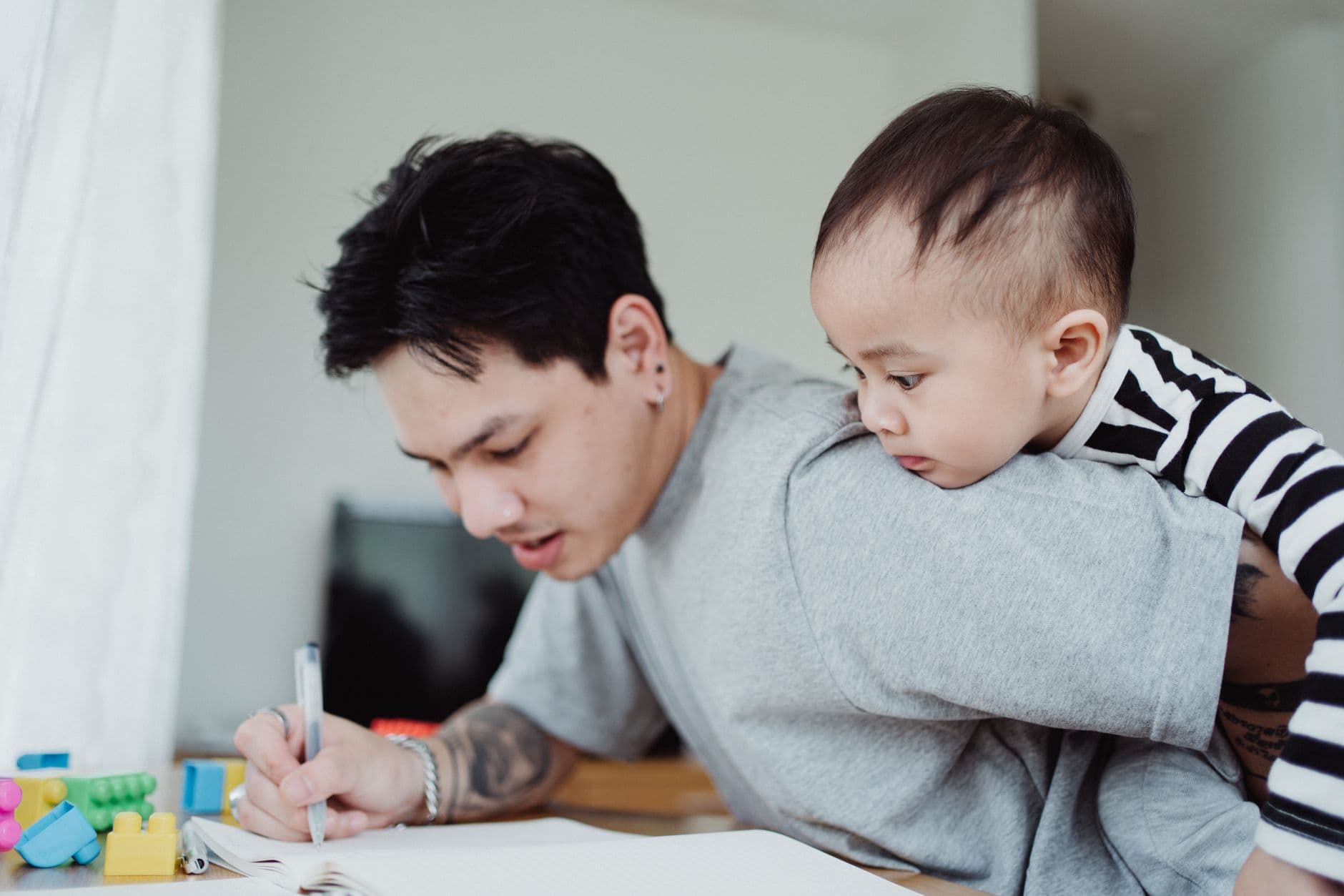 A father multitasking work while carrying his child, highlighting parenthood challenges.